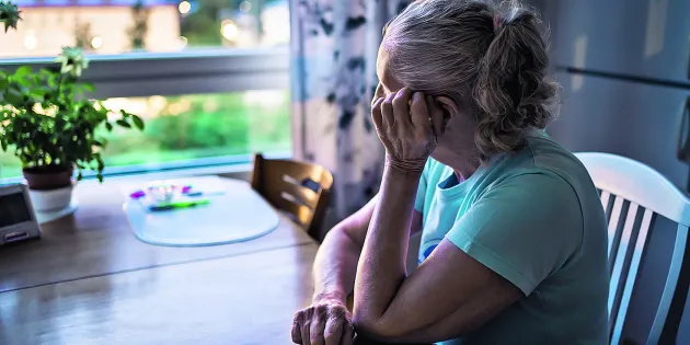 nainen istuu käsi poskella pöydän ääressä