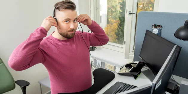 Sairaanhoitaja Henri Kelahaara istuu työpisteessään luurit päässä valmiina neuvomaan soittajia.